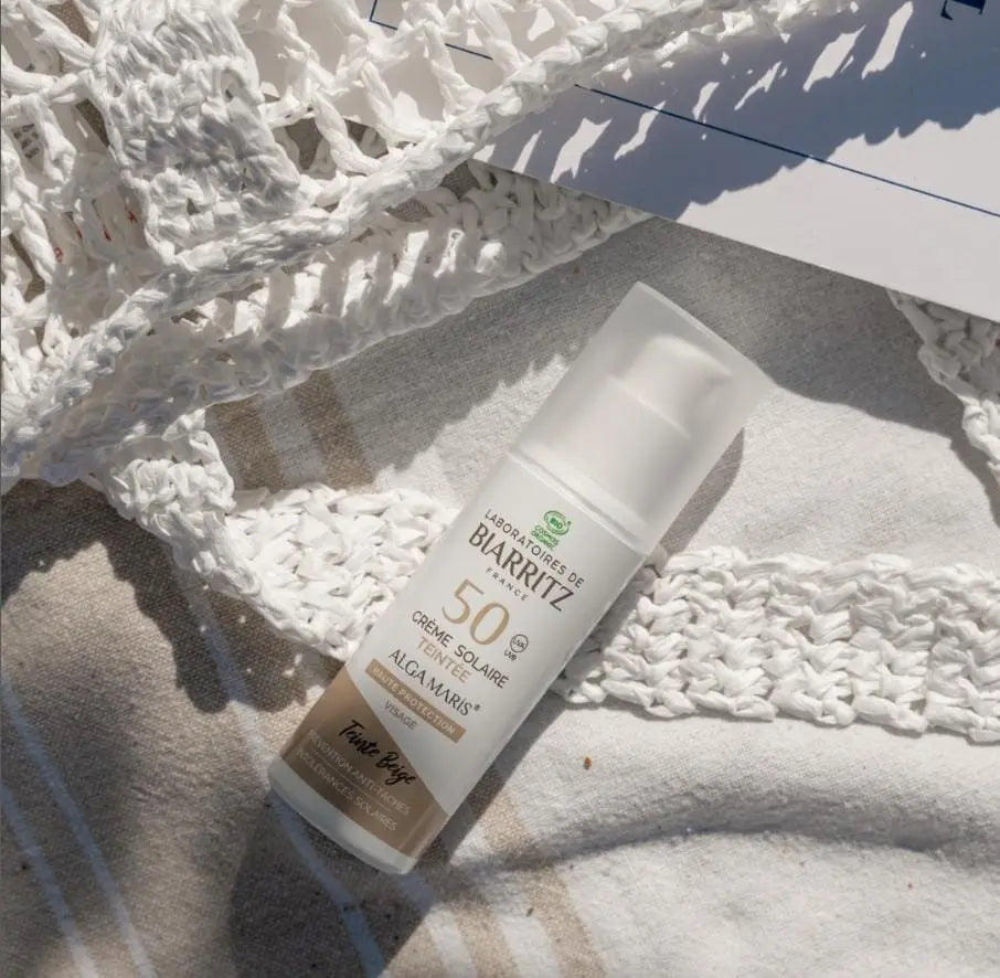 Laboratoires de Biarritz Alga Maris SPF 50 ansiktskrem ligger på en strandduk. Økologisk, vannfast og hudvennlig solkremer og solbeskyttelse med naturlige ingredienser for trygg soling.