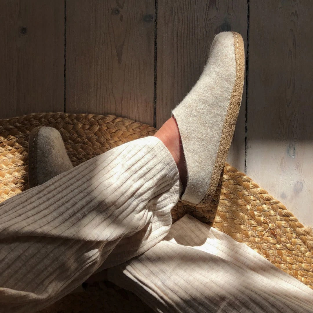 Lyse ulltøfler med gummisåle fra The Cozy Sheep på føtter i lune omgivelser. Naturlige, komfortable innesko i skandinavisk stil – ideelle for varme og ro året rundt