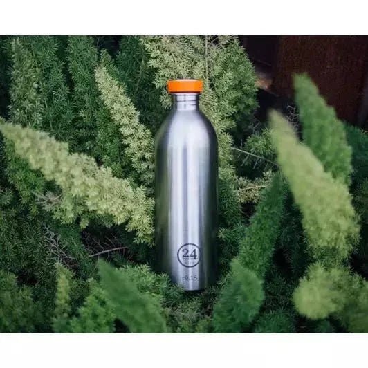 24Bottles Urban Drikkeflaske 500 ml Steel i rustfritt stål, med oransje kork, plassert i grønne planter