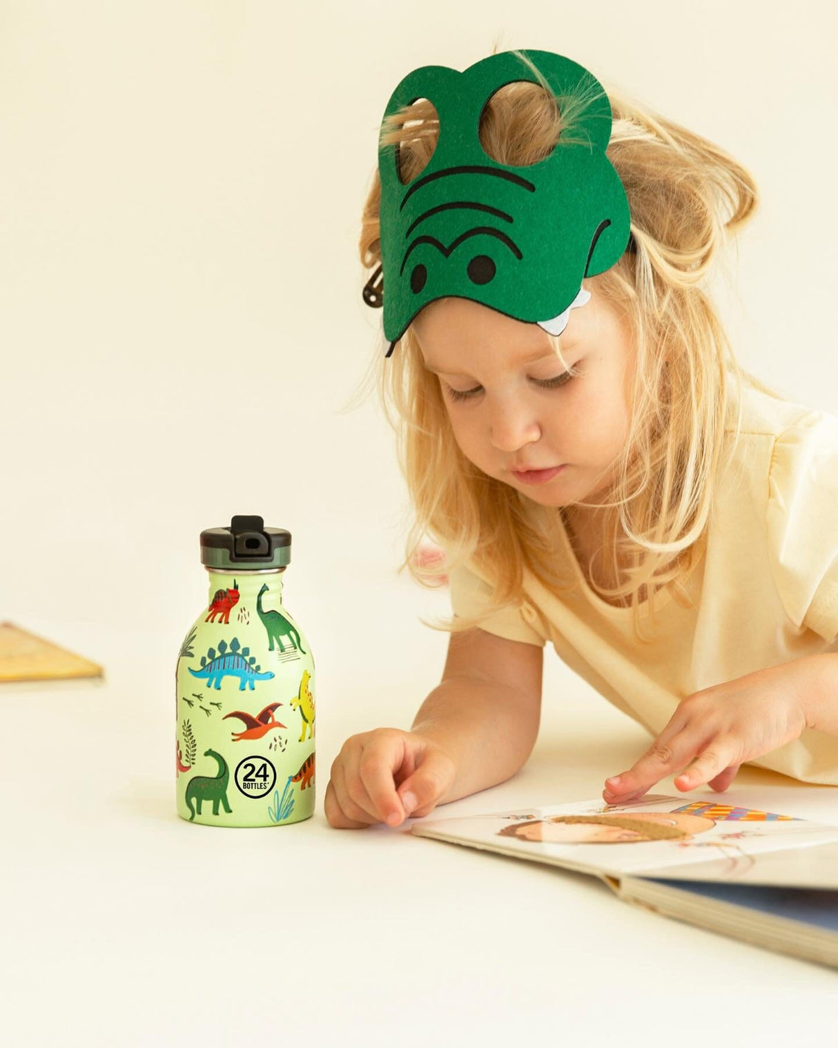 24Bottles Urban drikkeflaske barn 250 ml med dinosaurmønster ved siden av barn som leser bok