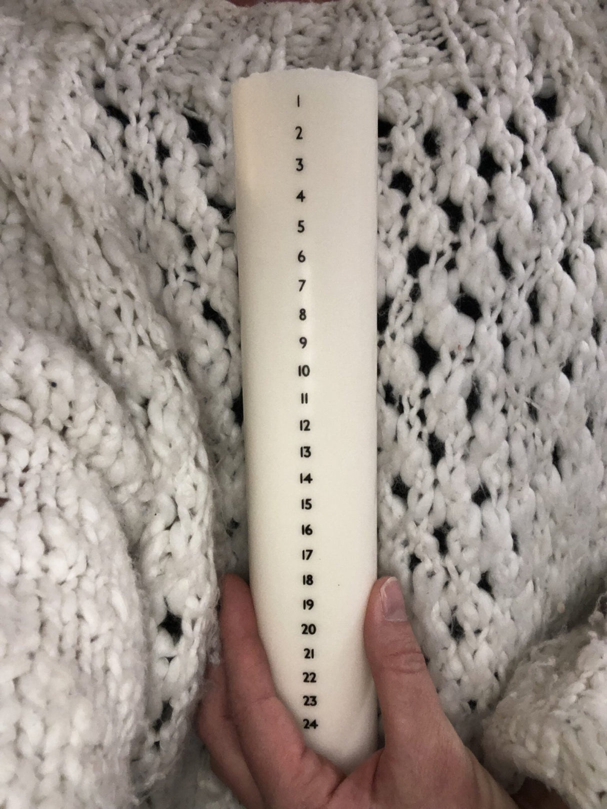 Åbenlys Kalenderlys Kubbelys 25 cm i hvit stearin og soyavoks, holdt i en hånd mot strikket bakgrunn