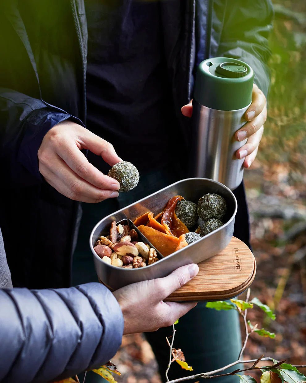 black+blum Bento-boks 1L med bambuslokk i rustfritt stål, i bruk sammen med en termokopp i skogen