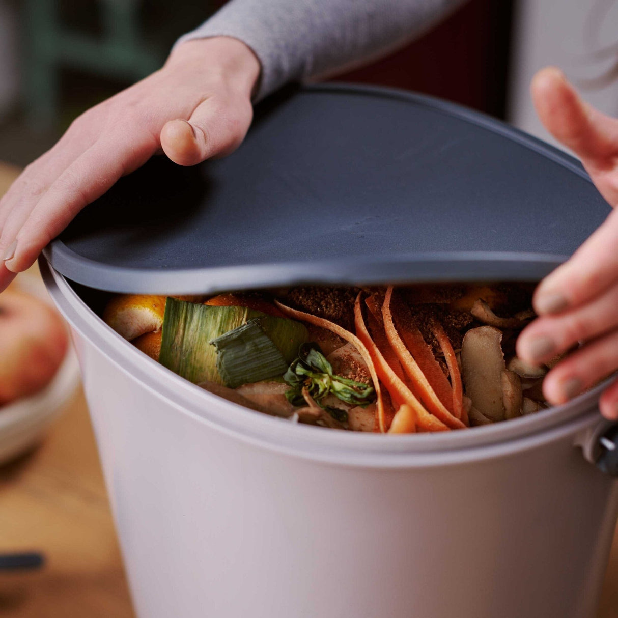 Bokashi Essence Kompostbøtte i grå plast med svart lokk og matavfall, nærbilde av fylling