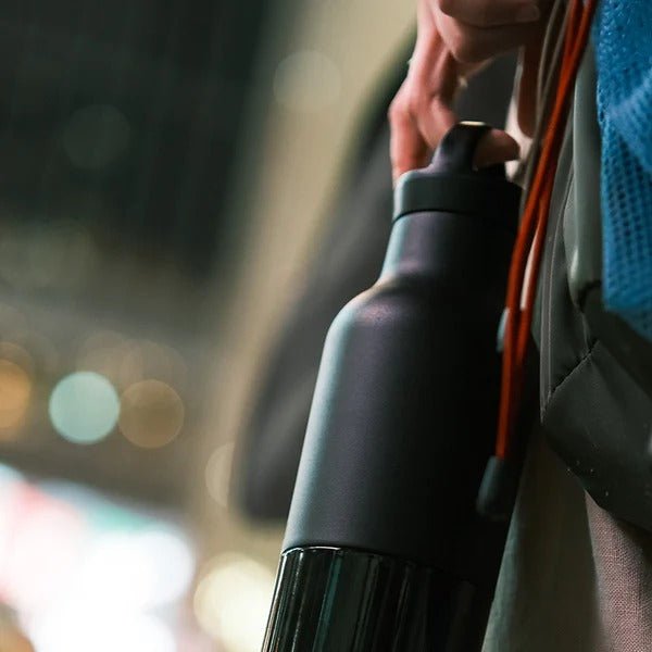 Klean Kanteen Classic Arch Loop Cap i svart polypropylen, en flaske holdt i hånden med bakgrunnslys