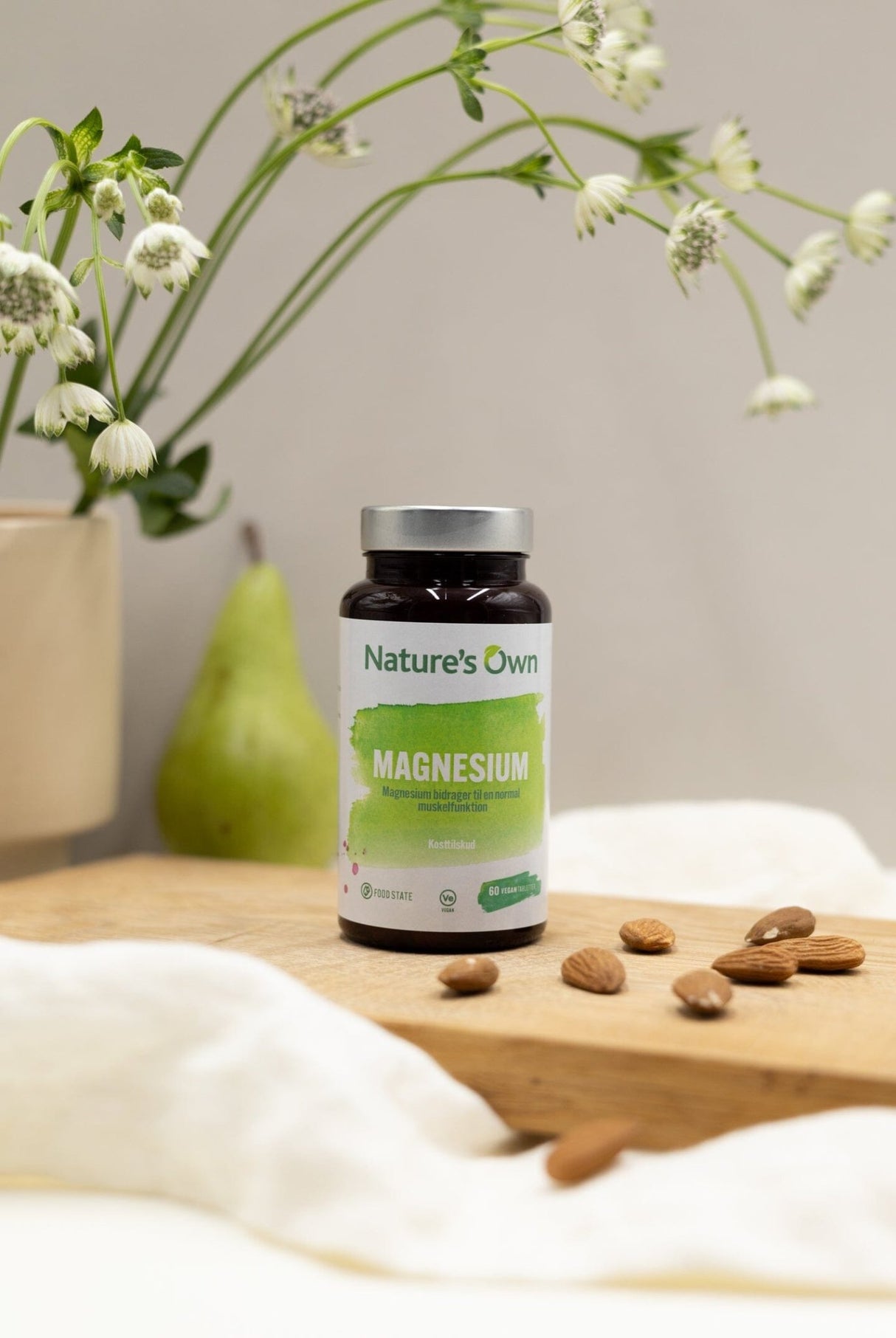 Natures Own Magnesium 60 tabletter i brun glassflaske med grønn etikett, på trebrett med mandler