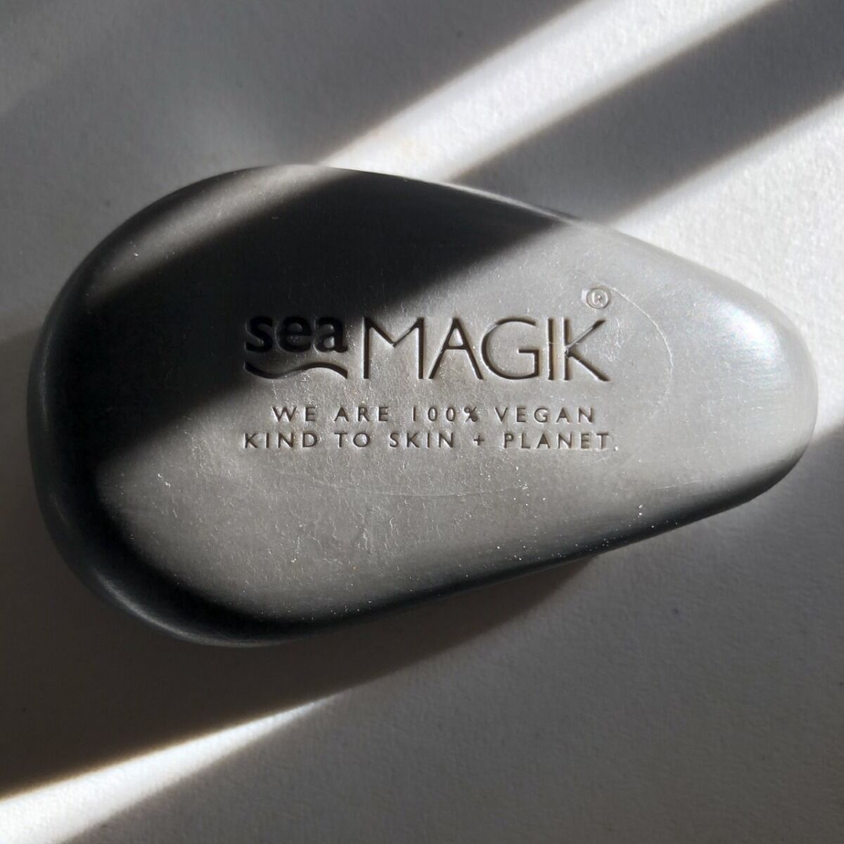 Sea Magik Black Mud Soap 100g, grå fast såpebar med logo preget i overflaten, sett ovenfra med skygger