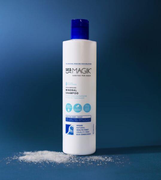 Sea Magik Mineral Sjampo 300 ml hvit i plastflaske med blå kork, med havsalt spredt på blå bakgrunn