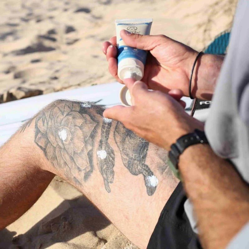 Suntribe Mineral Solkrem SPF 50, 100 ml, beige og blå i tube, i bruk på en tatovert legg på stranden