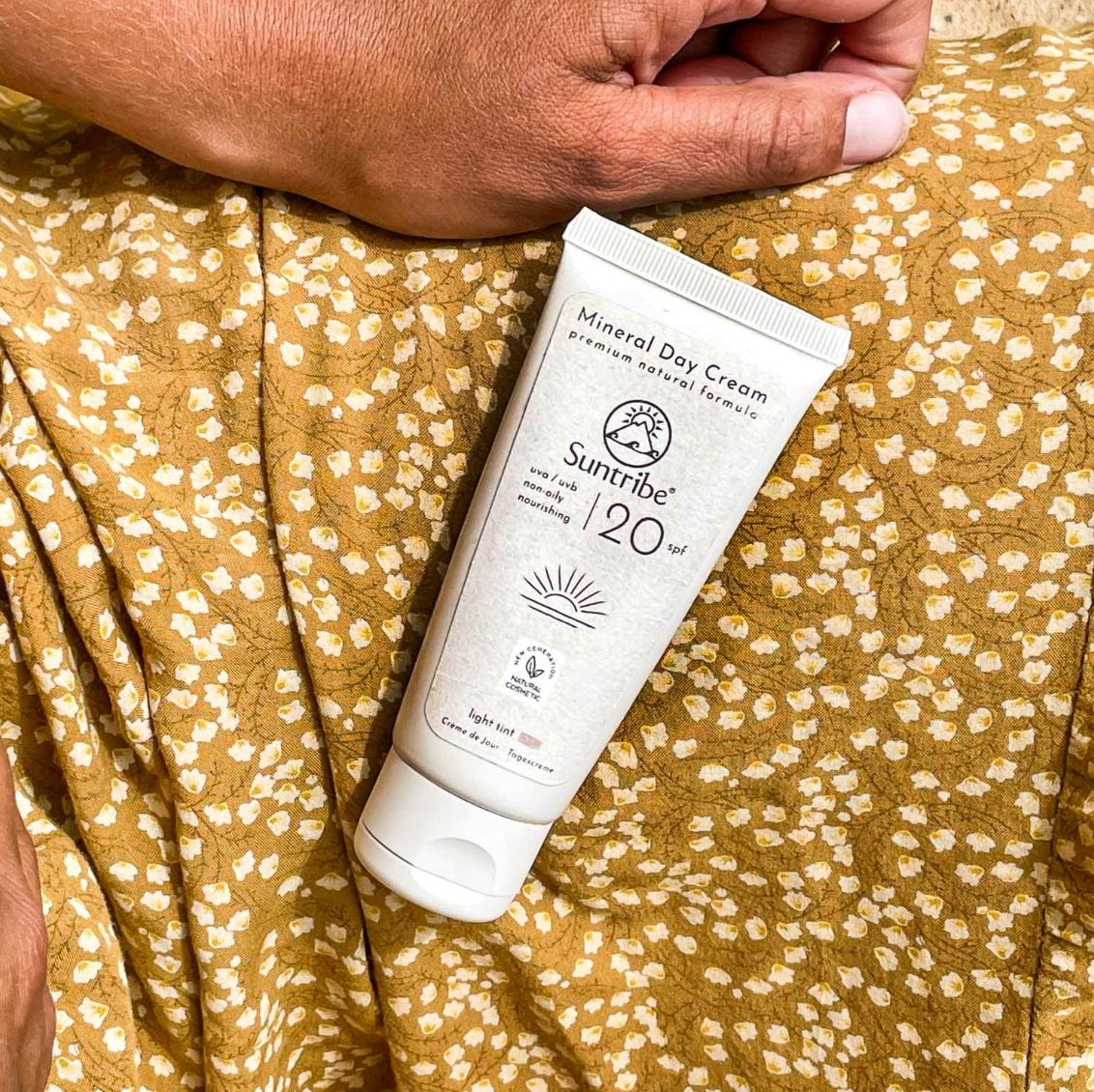 Suntribe Ansiktskrem med solfaktor SPF 20 Tinted 50 ml i plasttube, liggende på et blomstret stoff