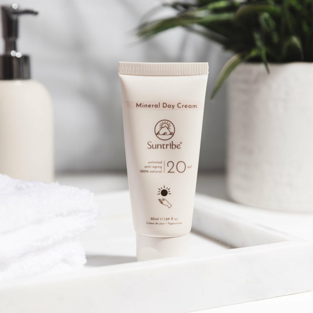 Suntribe Ansiktskrem SPF 20 Untinted 50 ml i kremform, hvit tube på en hvit hylle med grønn plante i bakgrunnen