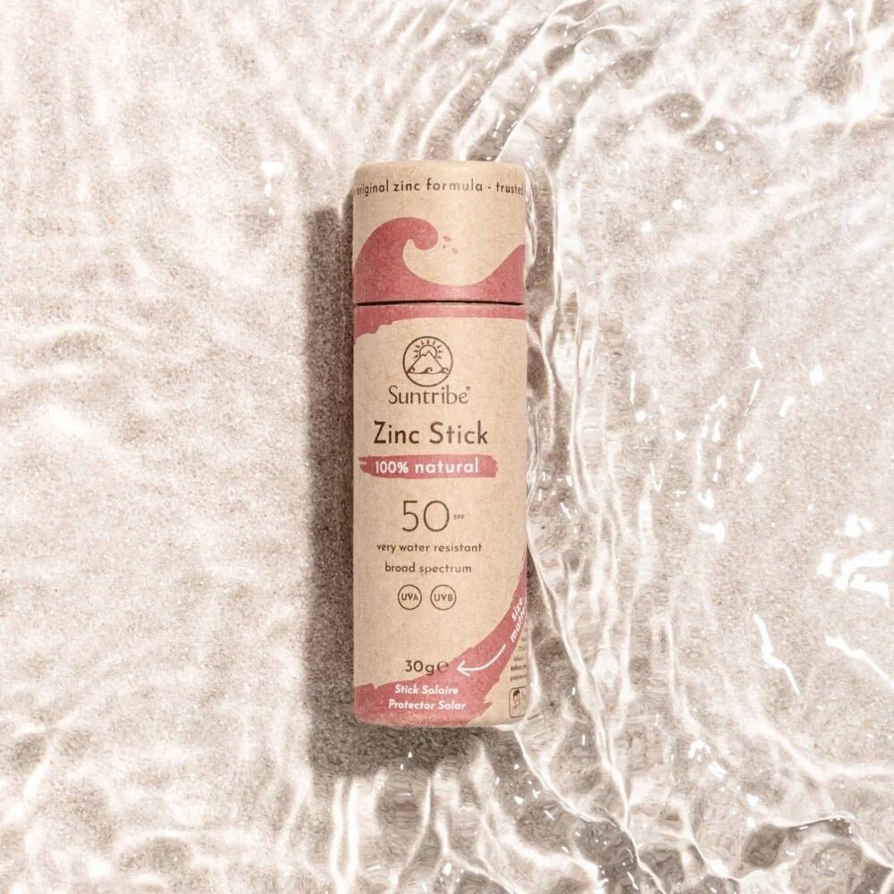 Suntribe solstift SPF 50 Pretty Pink i pappemballasje, sett ovenfra i vann på sandbunn