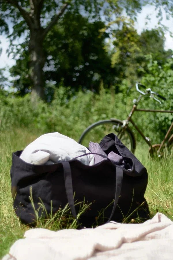 The Organic Company Big Long Bag veske, sort i økologisk bomull, i bruk på gress med sykkel i bakgrunn