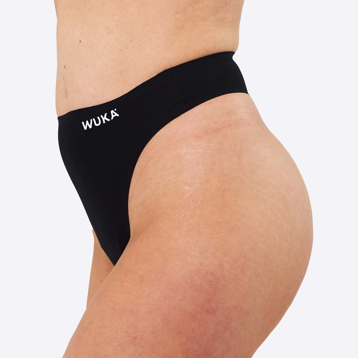 WUKA Stretch Thong Light/Medium flow svart i tekstil, modell iført trusen sett fra skrått bakfra
