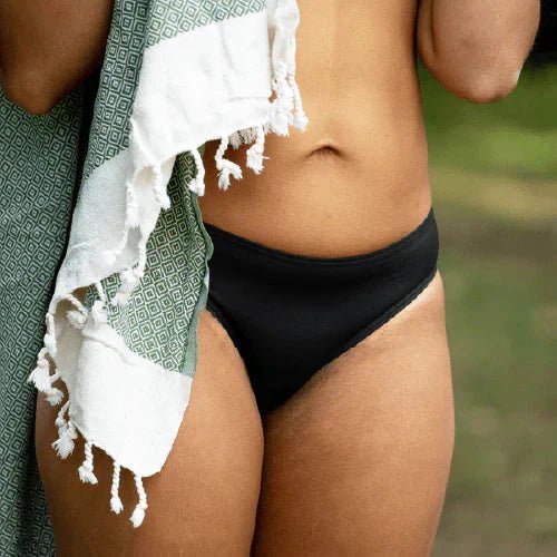 WUKA Swim Bikini Brief Light Flow Svart i stoff, i bruk på en person med håndkle over skulderen