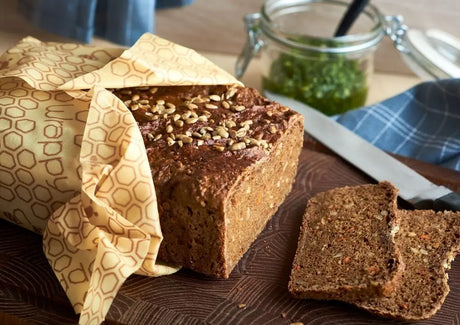 Bivokspapir omslutter nybakt brød på et skjærebrett. Plastfri, gjenbrukbar matoppbevaring som holder maten fersk og reduserer matsvinn.