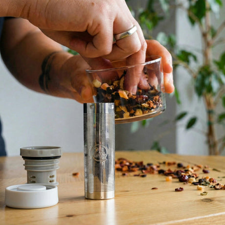 24Bottles Infuser lokk i grå og hvit plast og rustfritt stål, i bruk på et trebord med løs te