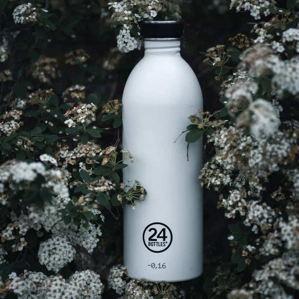 24Bottles Urban Drikkeflaske 1000 ml Ice White i rustfritt stål, stående blant grønne blader og hvite blomster