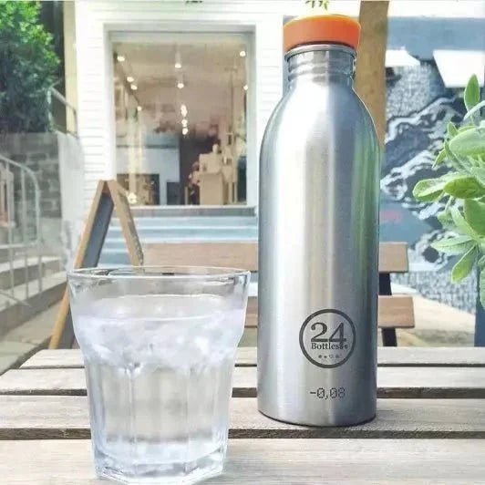 24Bottles Urban Drikkeflaske 500 ml Steel i rustfritt stål, med et glass vann på et trebord
