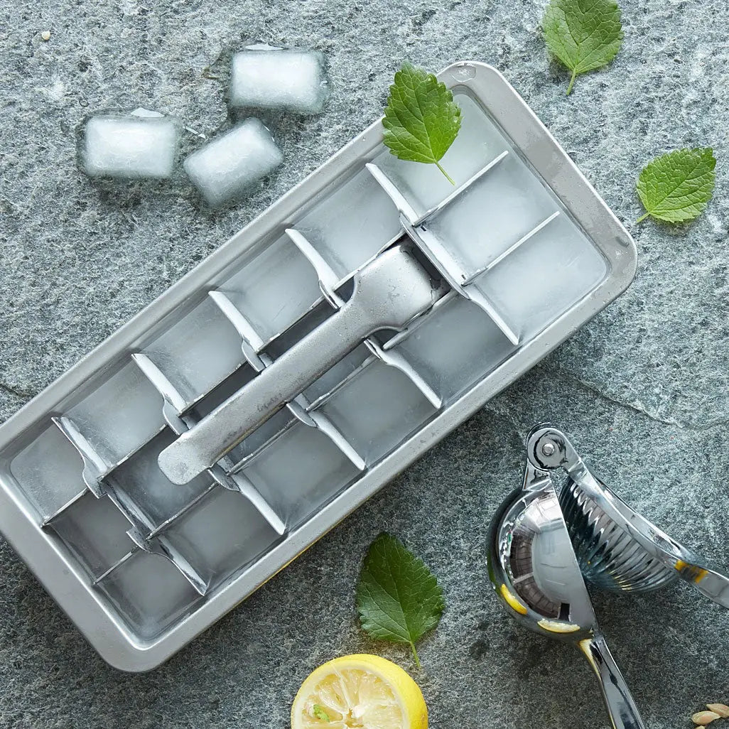 Isbitform i rustfritt stål med ferdige isbiter, sitron og mynte på kjøkkenbenk – perfekt til kalde drikker.