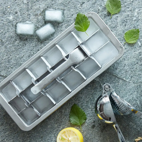 Isbitform i rustfritt stål med ferdige isbiter, sitron og mynte på kjøkkenbenk – perfekt til kalde drikker.