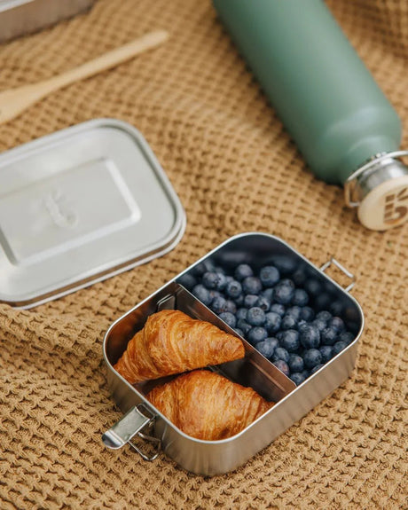 Bambaw Drikkeflaske 750ml Sage Green i rustfritt stål, liggende ved en matboks med croissanter