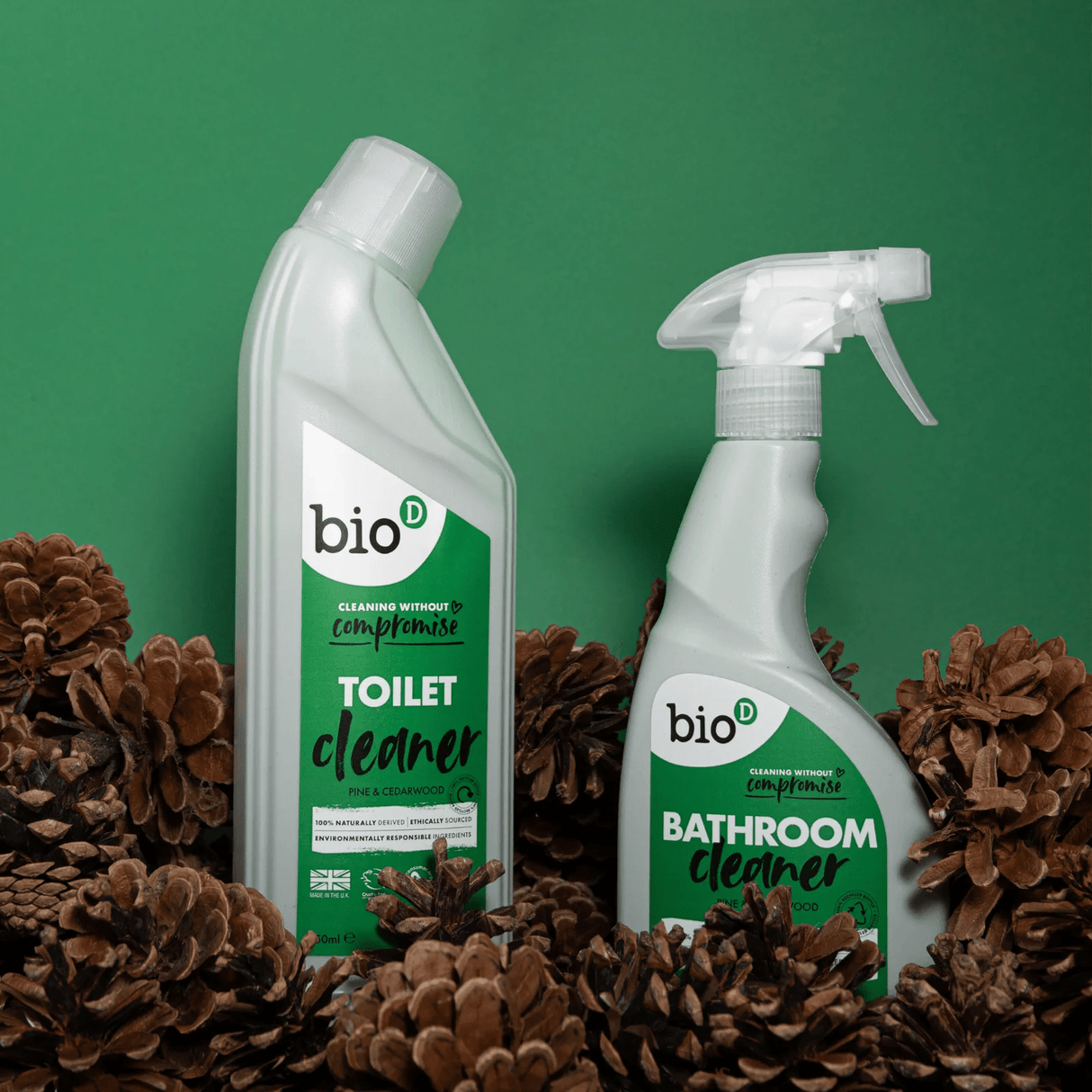 Bio-D toalettrens 750ml i hvit flaske med grønn etikett omgitt av kongler mot grønn bakgrunn