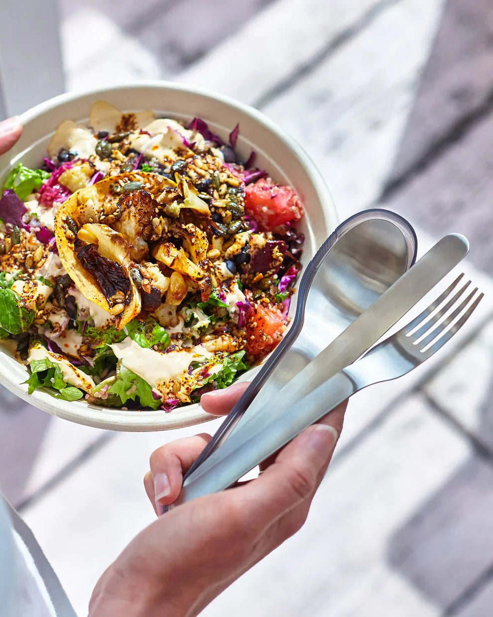 black+blum bestikksett i grå og sølv i rustfritt stål og silikon, holdt i hånden med en salatbolle