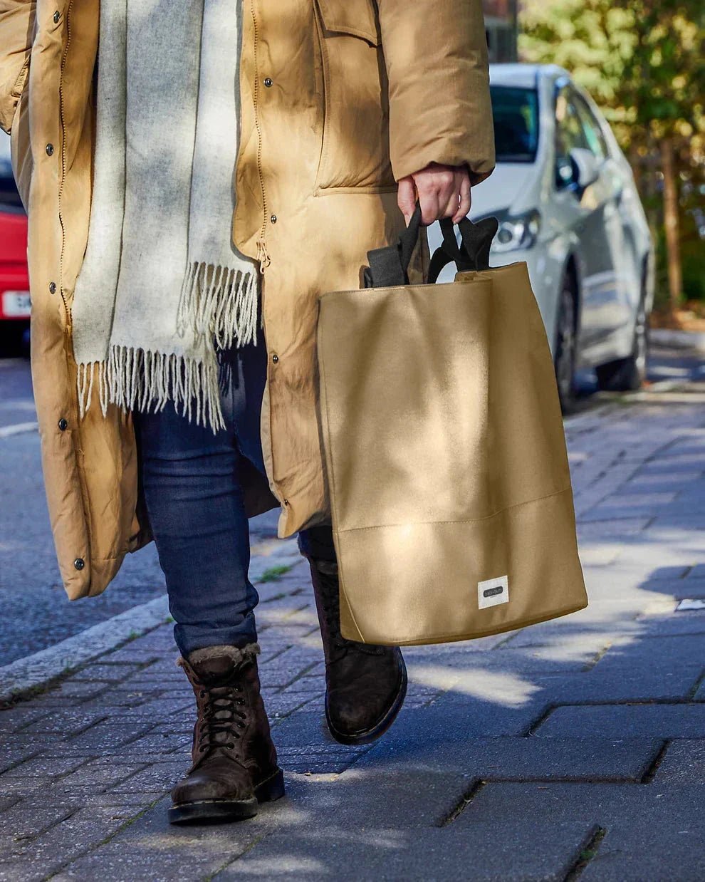 Black+Blum isolert handlenett Slate i polyester, båret i hånden av en person som går på fortauet