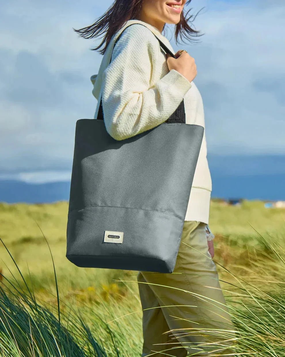 Black+Blum isolert handlenett Slate i polyester, i bruk på stranden med en person som bærer den over skulderen