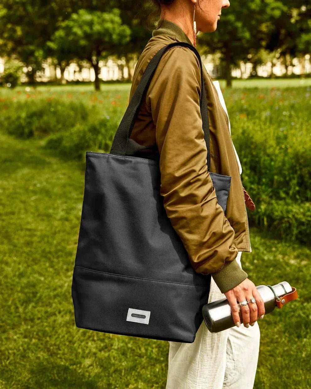 Black+Blum isolert handlenett Slate i polyester, båret over skulderen av en person i en park