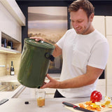 Bokashi Kompostbøtte 2.0 khaki i plast, en mann tapper væske fra bøtten ned i et glass på kjøkkenbenken