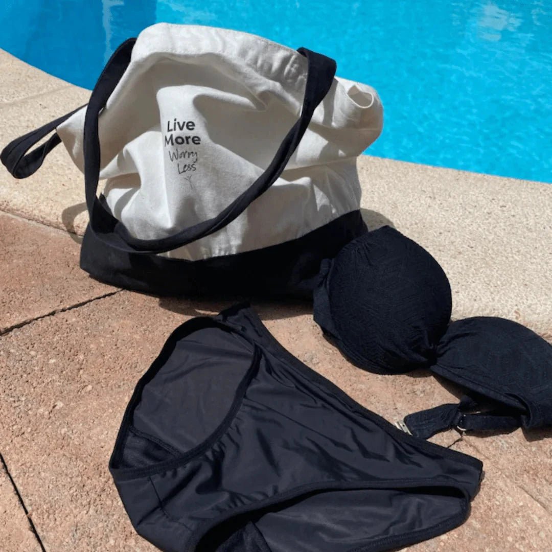 Comfydence Sunshine Bikini menstruse, svart, i stoff, sammen med en bikini-topp og handlenett ved bassengkanten