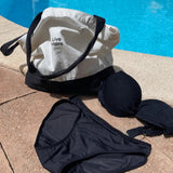 Comfydence Sunshine Bikini menstruse, svart, i stoff, sammen med en bikini-topp og handlenett ved bassengkanten
