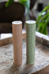 Kunstindustrien kalenderlys i Moss Green og Hazelnut, to varianter side ved side på et treunderlag