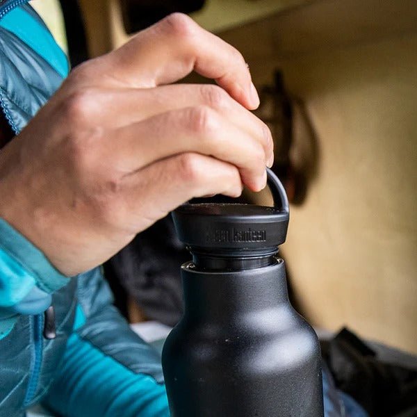 Klean Kanteen Classic Arch Loop Cap i svart polypropylen, en hånd som holder lokket på en flaske