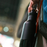 Klean Kanteen Classic Arch Loop Cap i svart polypropylen, en flaske holdt i hånden med bakgrunnslys