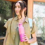 Klean Kanteen termoflaske 592 ml Pink Lemonade i rustfritt stål, holdt i hånden av en kvinne med ryggsekk