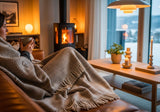 Læsø Garnspinderi ullpledd 140x240 cm i grå diagonal med frynser, i bruk på en sofa ved peisen