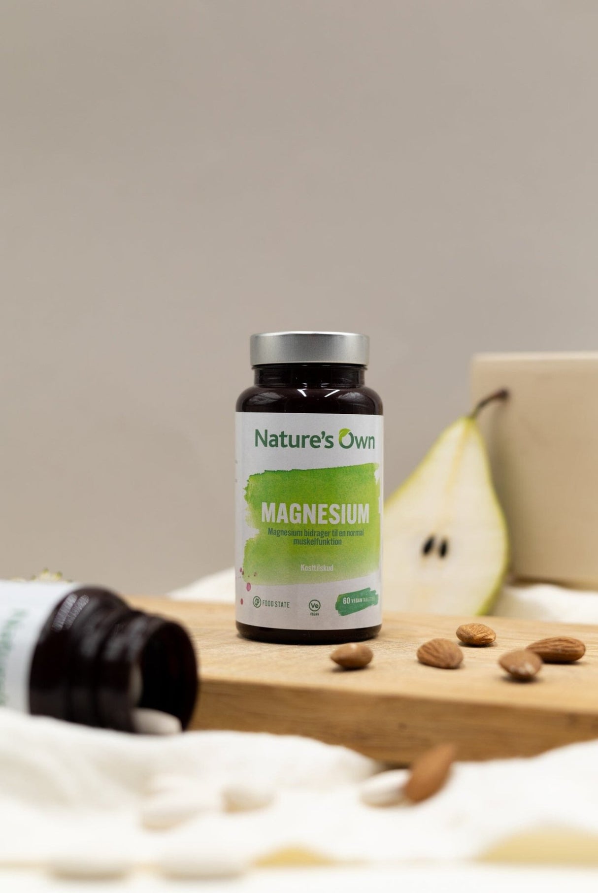 Natures Own Magnesium 60 tabletter i brun glassflaske med grønn etikett, med pære i bakgrunnen