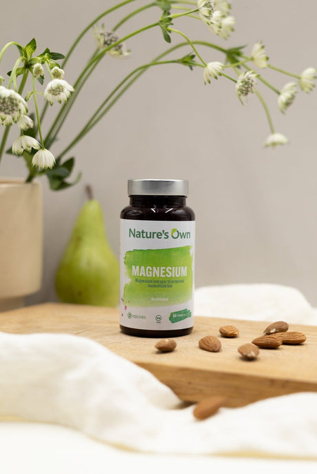 Natures Own Magnesium 60 tabletter i brun glassflaske med grønn etikett, på trebrett med mandler