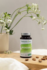 Natures Own Magnesium 60 tabletter på treplate med mandler og hvite blomster i bakgrunnen