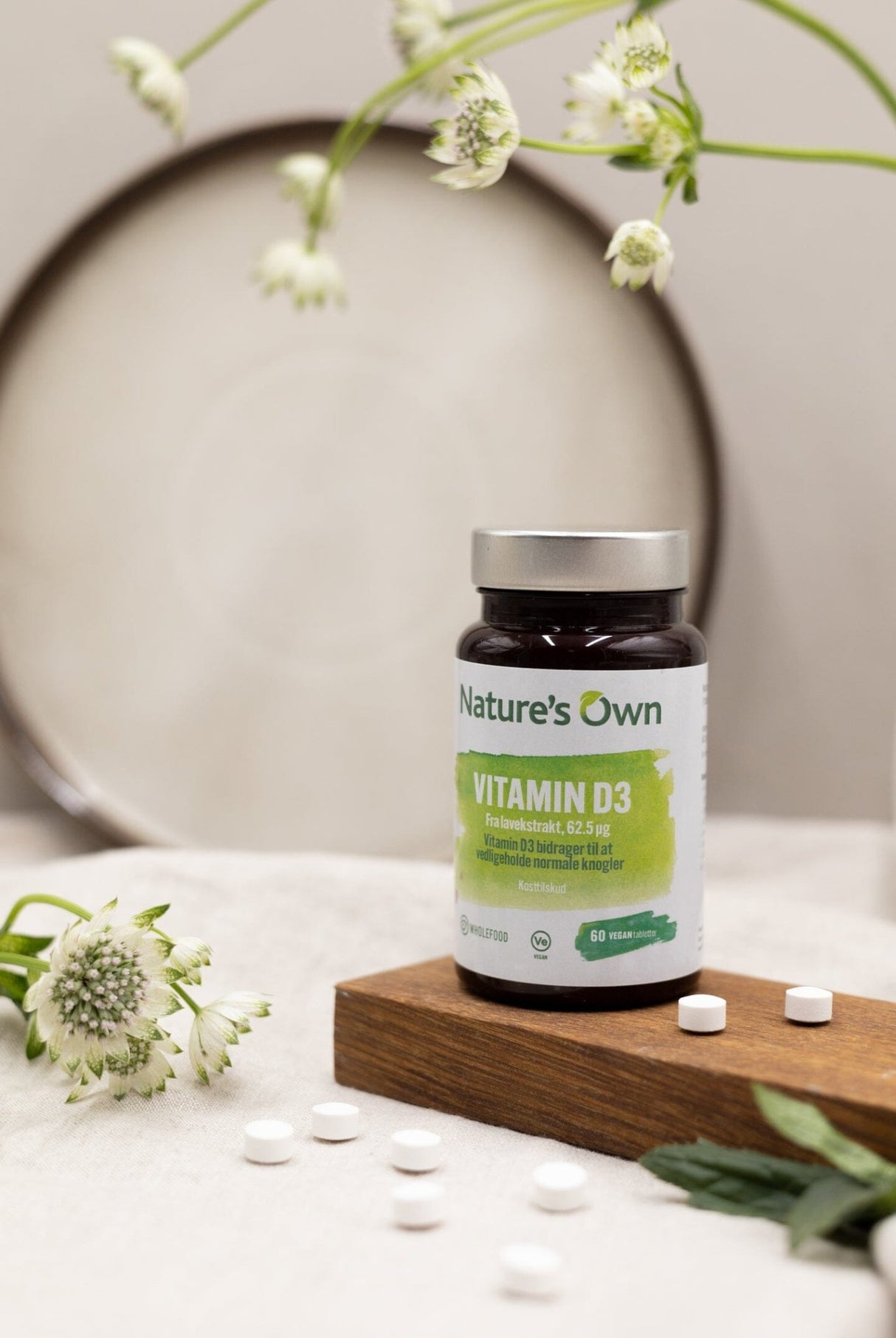 Natures Own Vitamin D3 60 tabletter i brun flaske med grønn etikett på treplate med tabletter spredt rundt