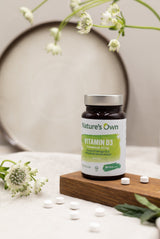 Natures Own Vitamin D3 60 tabletter i brun flaske med grønn etikett på treplate med tabletter spredt rundt