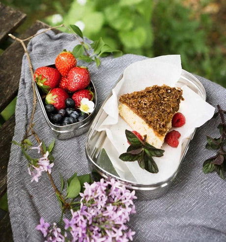 Pulito matboks oval 700 ml sølv i rustfritt stål med kake og bær på et grått pledd