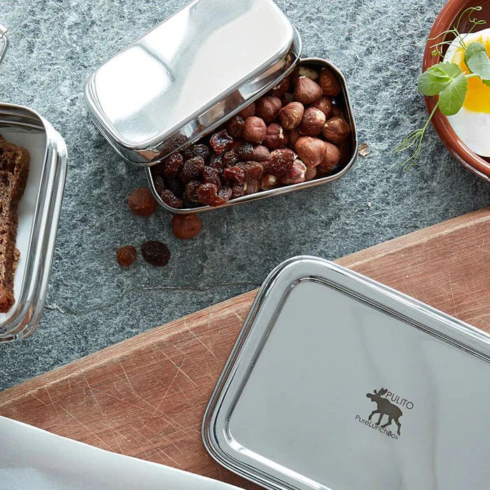 Pulito PureSnackBox 150 ml sølv i rustfritt stål, fylt med nøtter og rosiner på et bord