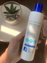Sea Magik Silky Smooth Body Lotion 300ml hvit i plast, holdt i en hånd med en plante i bakgrunnen
