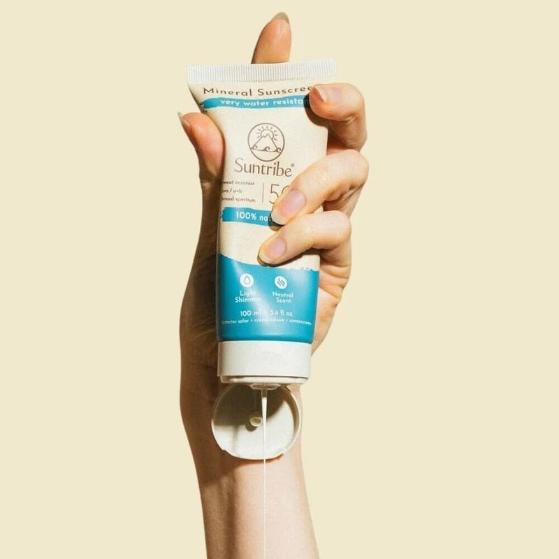 Suntribe Mineral Solkrem SPF 50, 100 ml, beige og blå i tube, holdt i en hånd som klemmer ut krem