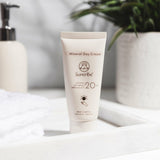 Suntribe Ansiktskrem SPF 20 Untinted 50 ml i kremform, hvit tube på en hvit hylle med grønn plante i bakgrunnen