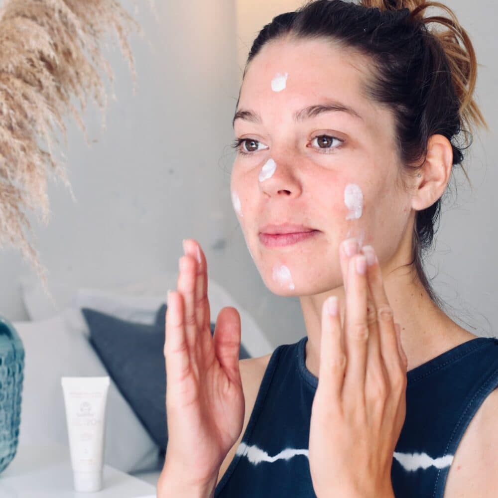 Suntribe Ansiktskrem SPF 20 Untinted 50 ml i kremform, påført i ansiktet på en kvinne, med kremtube i bakgrunnen
