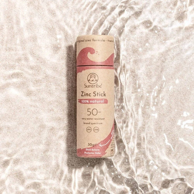 Suntribe solstift SPF 50 Pretty Pink i pappemballasje, sett ovenfra i vann på sandbunn Suztain.no